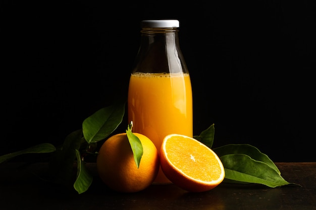 Una botella de jugo de naranja y una naranja a la mitad sobre un fondo oscuro