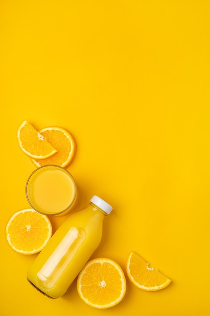 Botella con jugo y naranjas sobre un fondo amarillo.