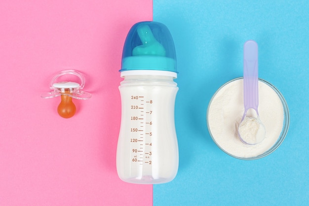 Botella de leche para bebé recién nacido, chupete sobre una superficie rosa y frasco con fórmula infantil en polvo sobre una superficie azul