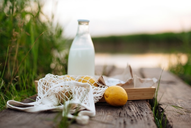 Una botella de leche y una bolsa de hilo con frutas sobre tablas de madera en el lago