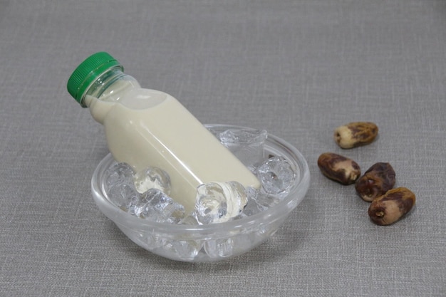 Una botella de leche de dátiles servida en una vista lateral del tazón de cubo helado sobre fondo gris