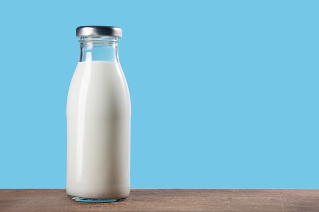 Botella de leche en una mesa de madera sobre un fondo azul.