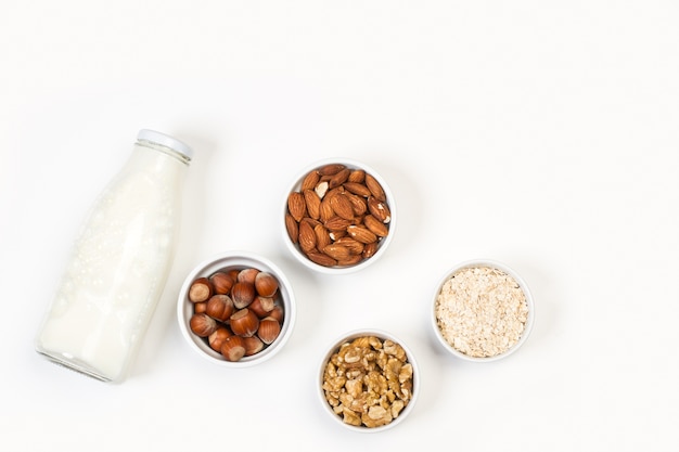 Una botella de leche con nueces en tazones blancos sobre un fondo blanco.