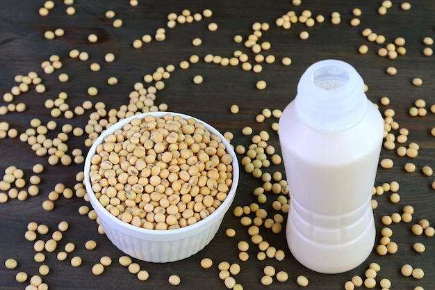 Botella de leche de soja en la mesa de madera negra con frijoles de soja dispersos