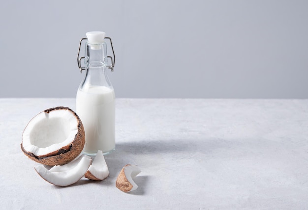 Botella de leche vegana de vidrio sobre mesa de mármol blanco con medio cocos. Vista frontal y copia de la imagen del espacio.