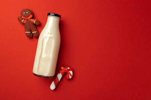 Botella de leche de vidrio y galletas de jengibre de Navidad sobre fondo rojo.