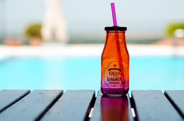 Botella de limonada fresca en la mesa de tablero de madera en el fondo de la piscina borrosa