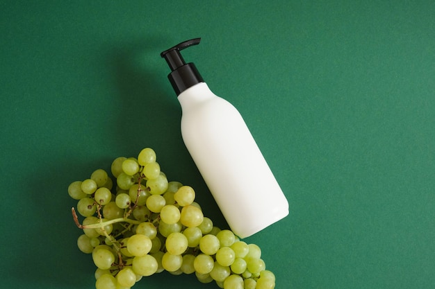 Botella de maqueta blanca con dispensador y uvas sobre fondo verde