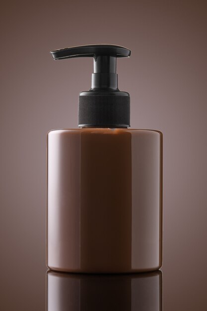 Foto botella marrón de jabón líquido o gel sobre un fondo de chocolate. una botella de jabón íntimo sobre vidrio.