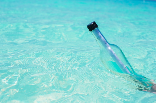 Botella con un mensaje en el cielo azul de fondo de mano