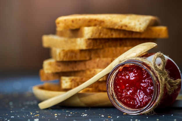 Botella de mermelada de fresa y pan de trigo integral se apilan en la mesa.