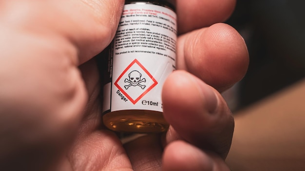 Foto botella de nicotina líquida en la mano con símbolo de advertencia de peligro en primer plano