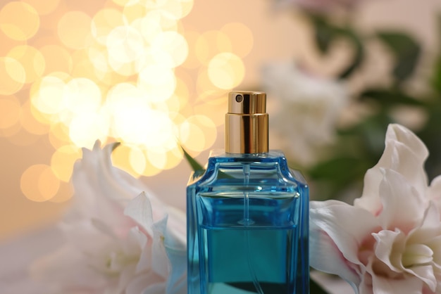 Botella de perfume y hermosas flores de lirio contra un fondo beige con luces borrosas de primer plano