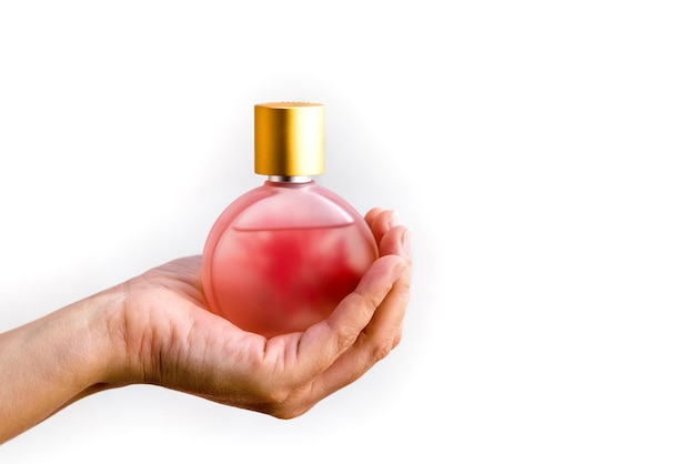 Botella de perfume en la mano de una mujer sobre un fondo blanco.
