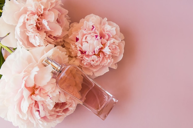 Una botella de perfume de mujer sobre un fondo rosa con una vista superior de peonía una copia del espacio el concepto de perfumería y belleza