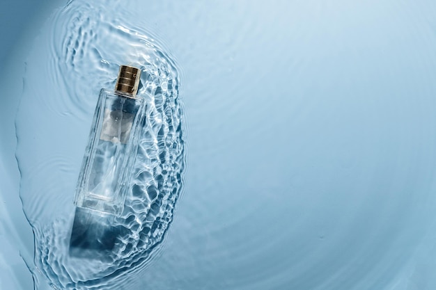 Botella de perfume sobre fondo ondulado de agua azul. Concepto de fragancia de mar fresco. Esencia de mujer y de hombre.