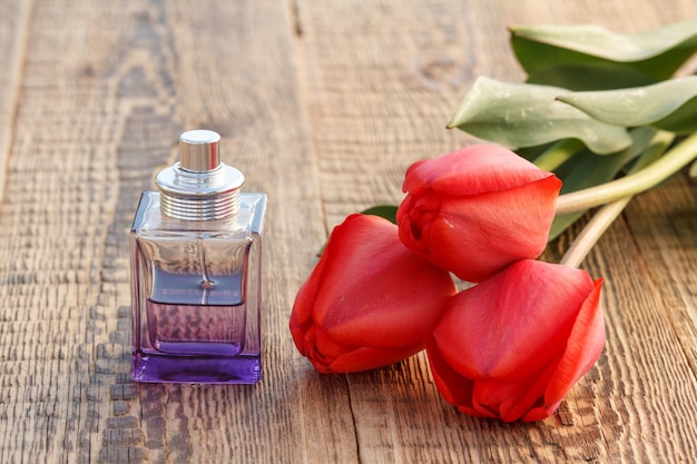 Botella de perfume sobre tablas de madera con tulipanes rojos.