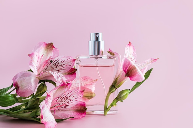 Una botella de perfume transparente y una composición elegante con flores de primavera sobre un fondo rosa vista frontal una presentación de aroma de espacio de copia