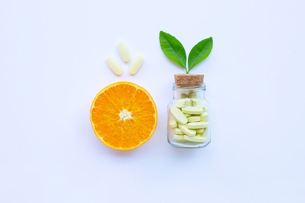 Botella y píldoras de la vitamina C con la fruta anaranjada en blanco.