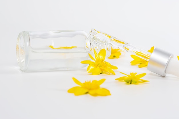 Una botella con una pipeta de suero sobre un fondo blanco rodeado de flores amarillas de primavera