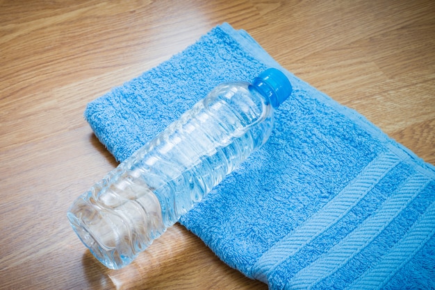 Botella plástica de agua y toalla en la mesa de madera.