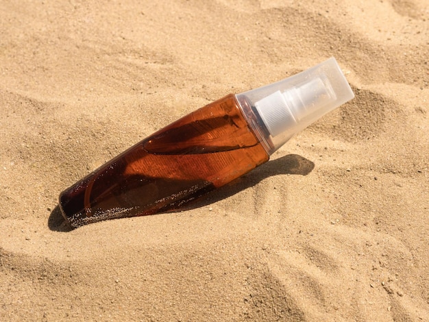 Una botella de plástico de aceite bronceador se encuentra en la arena bajo el sol brillante, un lugar para sombras duras de texto