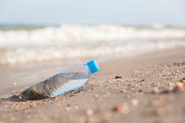 Botella de plástico con agua en el fondo de una playa de arena en un día soleado.