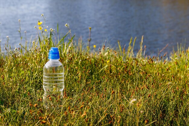 Botella de plástico con agua potable fresca en hierba verde en la orilla de un río