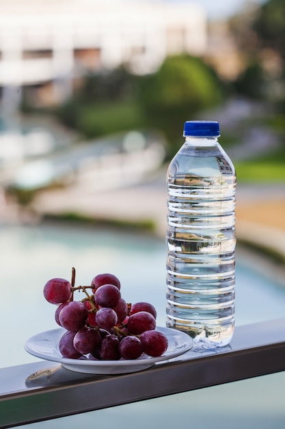 Botella de plástico con agua potable junto a las uvas maduras