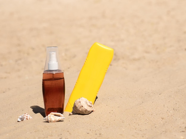Botella de plástico amarilla y aceite en una botella transparente en la arena bajo el sol brillante Sol de cosméticos