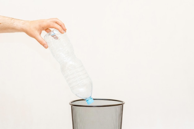 La botella de plástico se arroja a la canasta de basura para su eliminación y reciclajeFondo gris blancoespacio de copia de enfoque selectivo