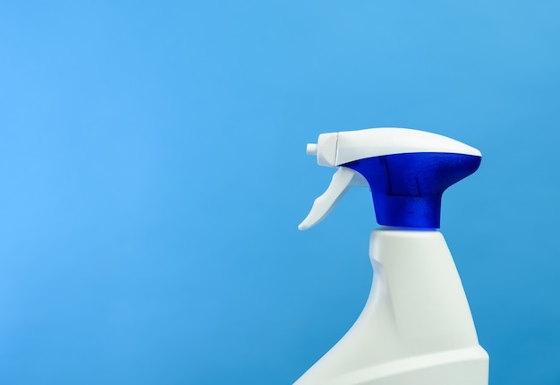 Botella de plástico blanco con boquilla de spray y espuma con detergente sobre fondo azul, espacio de copia