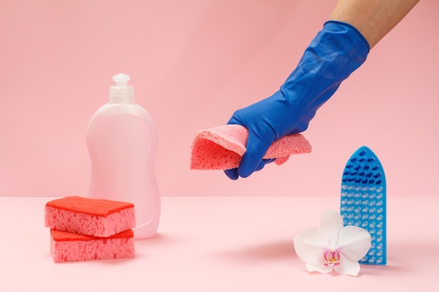 Botella de plástico de cepillo de esponjas líquidas para lavar platos y una mano en un guante de goma sosteniendo un trapo