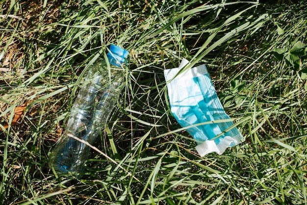 Botella de plástico y mascarilla protectora médica usada en basura de hierba verde en la naturaleza Concepto de contaminación ambiental