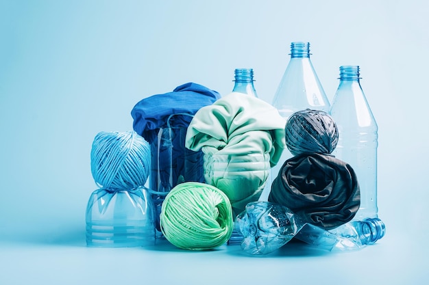 Botella de plástico vacía y varios tejidos hechos de tejido sintético de fibra de poliéster reciclado sobre un fondo azul.