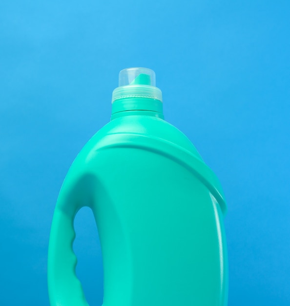 Botella de plástico verde con detergentes sobre fondo azul, cerrar