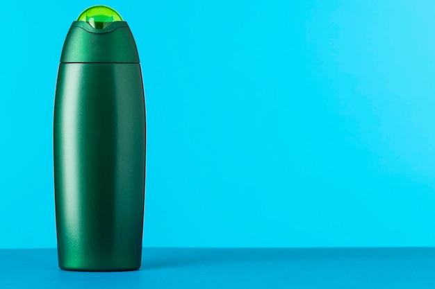 Una botella de plástico verde sin nombre para un producto cosmético sobre un fondo azul.