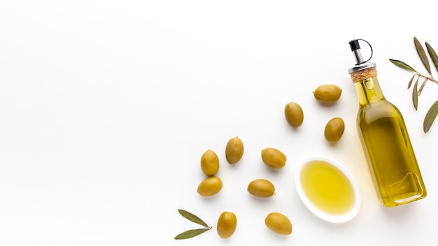 Botella y plato de aceite de oliva de alto ángulo con aceitunas amarillas y espacio de copia