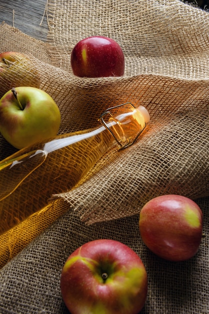 Una botella de primer plano de vinagre de sidra de manzana. Sidra y manzanas sobre arpillera.