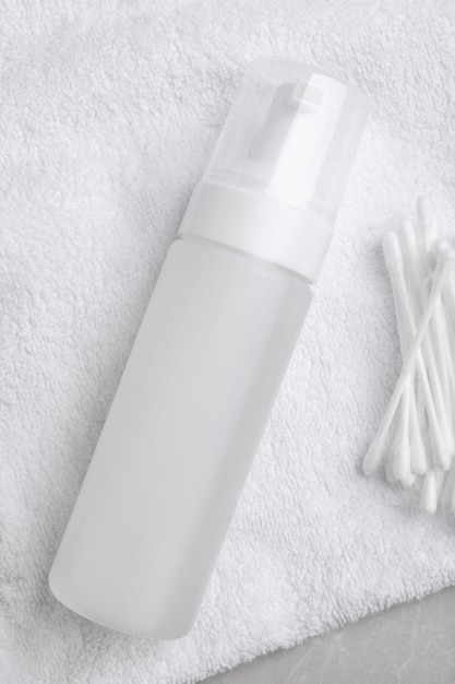 Botella de producto de limpieza facial y bastoncillos de algodón sobre una toalla blanca plana Espacio para texto