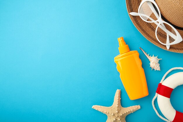 Botella de protección solar con sombrero, gafas y otros accesorios sobre fondo azul.