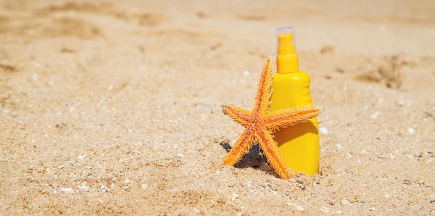 Botella de protector solar y una estrella de mar en la playa