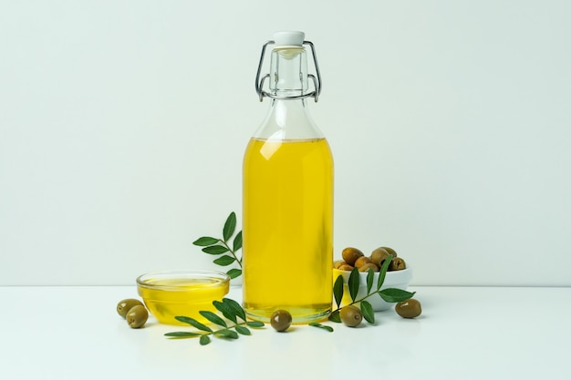 Botella y recipiente con aceite de oliva, aceitunas y ramitas sobre fondo blanco.