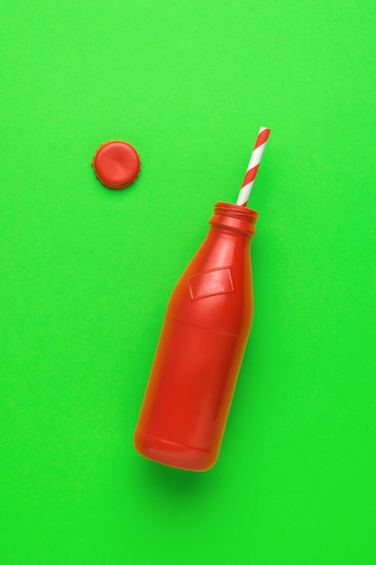 Una botella roja abierta y un tubo de cóctel sobre un fondo verde.