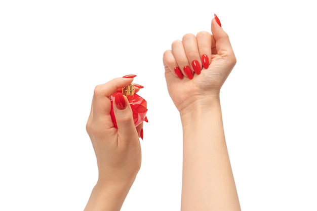 Botella roja de perfume en mano de mujer con uñas rojas aisladas en un fondo blanco