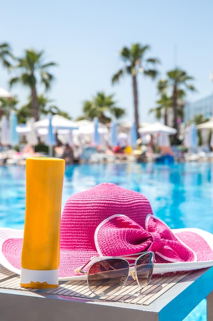 Botella de sombrero de crema solar y gafas de sol junto a la piscina en el hotel