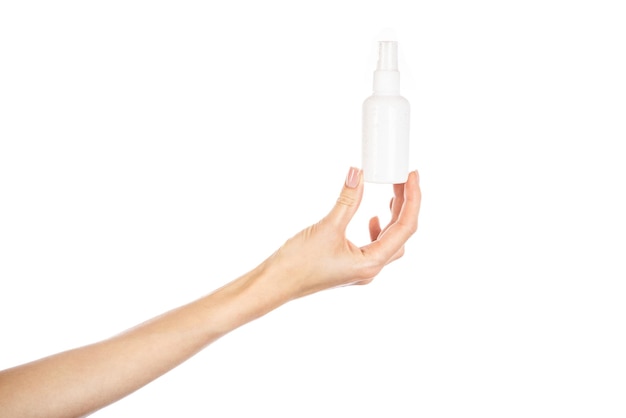 Botella de spray cosmético blanco en manos femeninas aislado sobre fondo blanco.