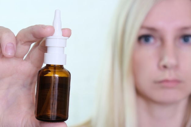 Una botella de spray nasal en la mano de una mujer de cerca, alergia, rinitis viral y bacteriana y tratamiento de la sinusitis.