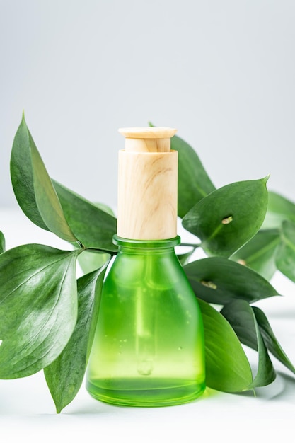 Botella de suero de vidrio esmerilado verde sobre fondo blanco con hojas verdes. Cosméticos naturales para el rostro, maquetas.Envases sin marca de productos para el cuidado de la piel.