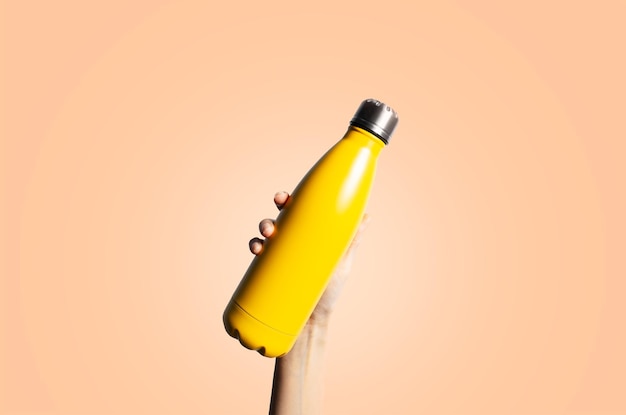 Botella térmica amarilla en la mano sobre un fondo de color del año pelusa de melocotón